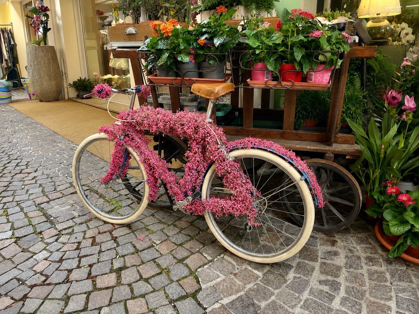 Blumengeschmücktes Fahrrad vor einem Blumenladen auf einem Kopfsteinpflaster